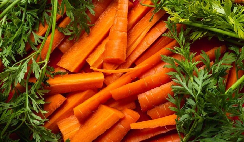Orange morötter med gröna blastdelar, fotograferade tätt uppifrån